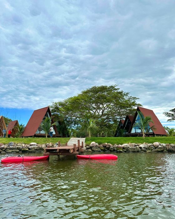 Cabañas triangulares de glamping en la orilla del río, con kayaks rojos en el agua